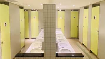 A public restroom with multiple sinks and toilets, a tiled wall, and a central pillar.