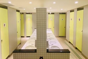 En offentlig toilet med flere håndvaske og toiletter, en flisebelagt væg og en central søjle.