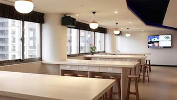 A modern kitchen with a long counter, stools, and a television on the wall.