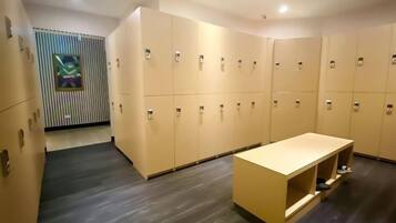 A hotel room with a wooden floor, a long beige bench, and a row of beige lockers.