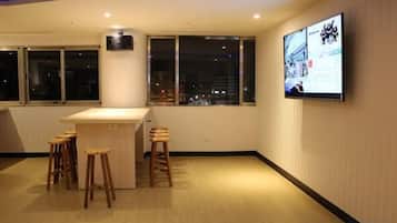 A room with a bar area, stools, a television mounted on the wall, and large windows.