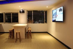 A room with a bar area, stools, a television mounted on the wall, and large windows. - Hey Bear Capsule Hotel (Xinbei Taipei Bridge Metro Station) (New Taipei City)