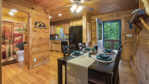 L’intérieur d’une cabane en bois comprend une table à manger pour quatre personnes, un coin cuisine et un ventilateur de plafond.