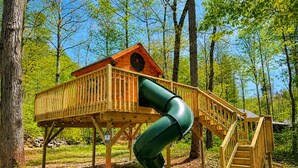 Une cabane en bois avec un toboggan et des escaliers, entourée d’arbres.