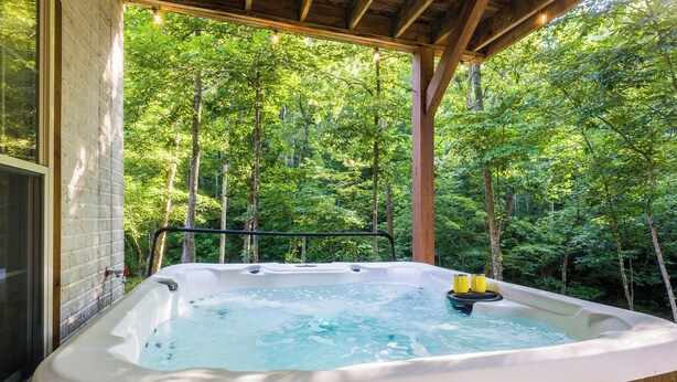 Un bain à remous installé sur une terrasse en bois, avec vue sur une forêt.