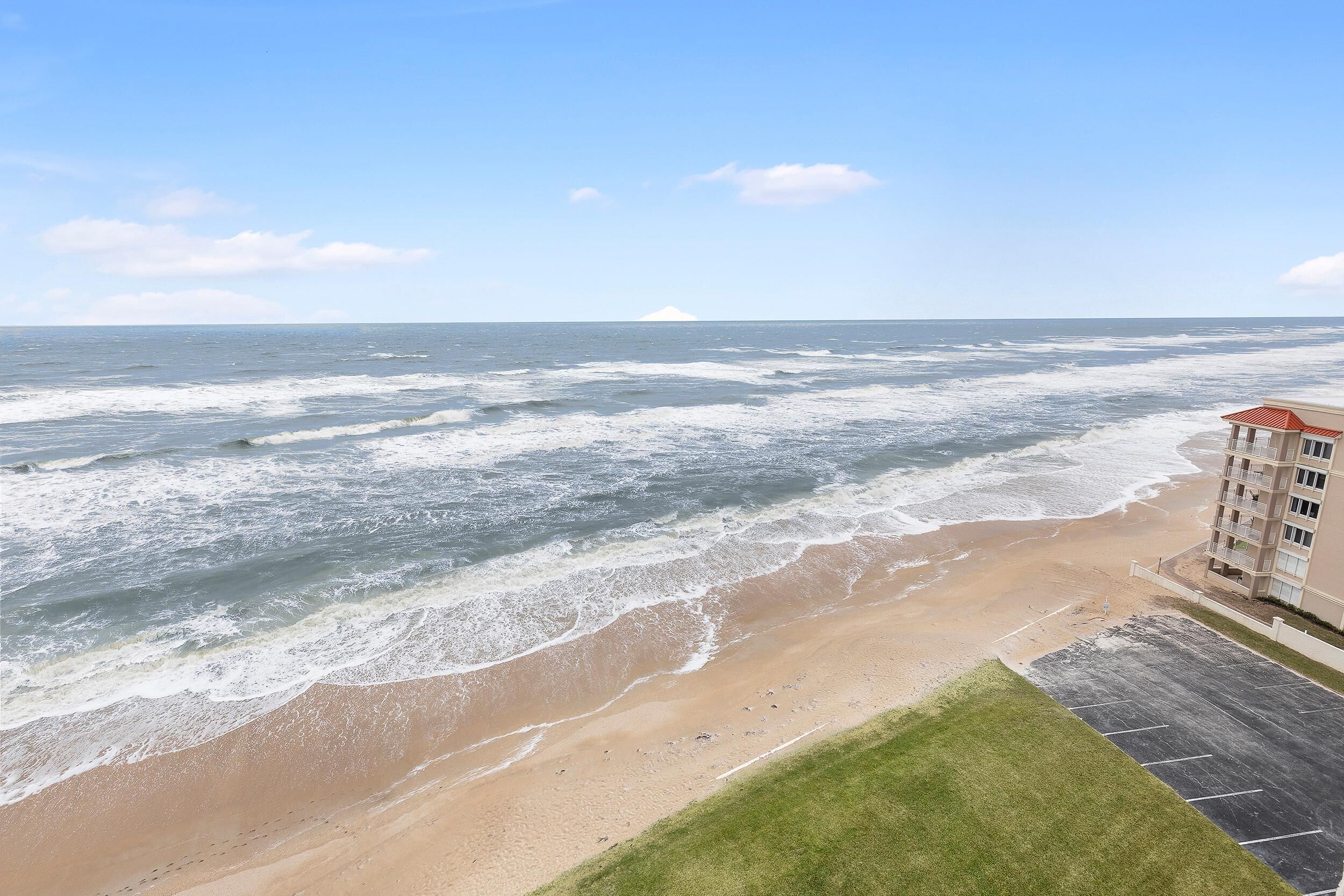 Une vue sur la plage avec des vagues, un parking et un bâtiment avec un toit rouge.