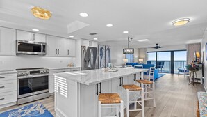 A modern kitchen with white cabinetry, a large island, and a view to the outside. - Southwind 1002 (New Smyrna Beach)