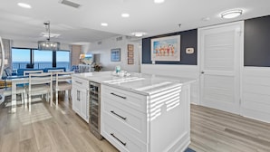 A modern kitchen with white cabinetry, a marble countertop, and a view of the ocean through large windows. - Southwind 1002 (New Smyrna Beach)