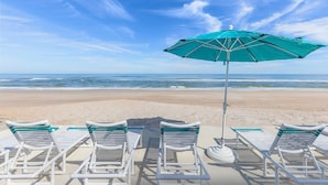 A beach with white lounge chairs and a green umbrella. - Southwind 1002 (New Smyrna Beach)