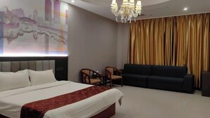 A hotel room with a large bed, a sofa, two chairs, a chandelier, and a wall with a cityscape mural.