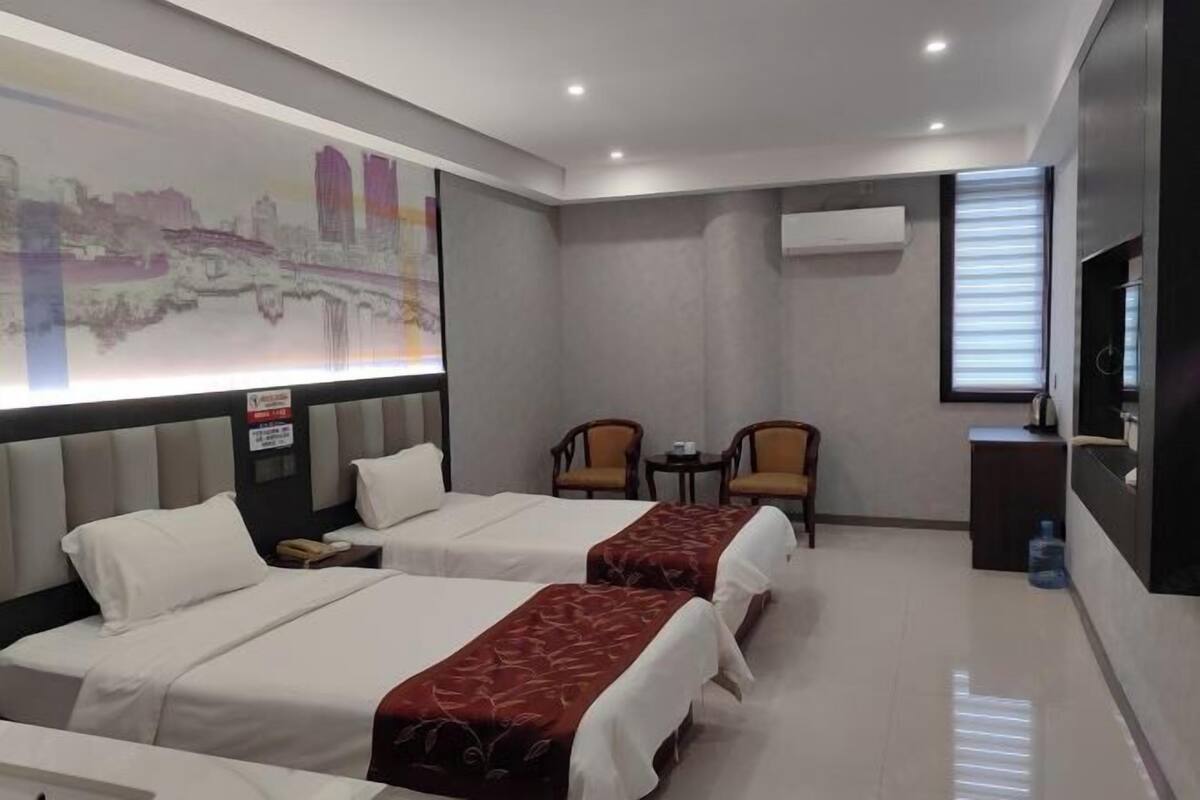 Habitación de hotel con dos camas, un escritorio, dos sillas, un televisor y un equipo de aire acondicionado.
