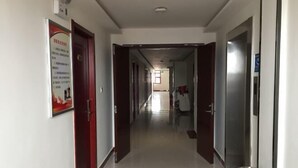 A corridor with doors on either side, a poster on the left wall, and a trash bin at the end.