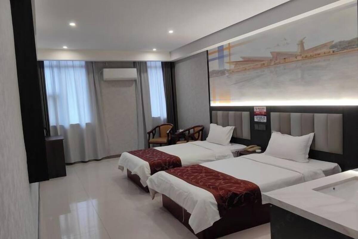 Una habitación de hotel con dos camas, un escritorio, una silla y un amplio ventanal con cortinas.