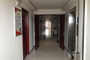A corridor with doors on either side, a poster on the left wall, and a trash bin on the right.