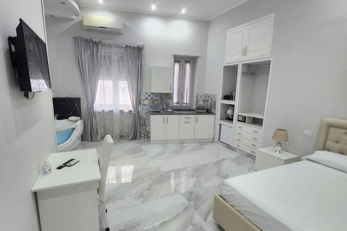 A modern bedroom with a large bed, a desk, a vanity, and a walk-in closet.