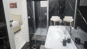 A modern bathroom with a white sink, black marble walls, and a glass shower enclosure.