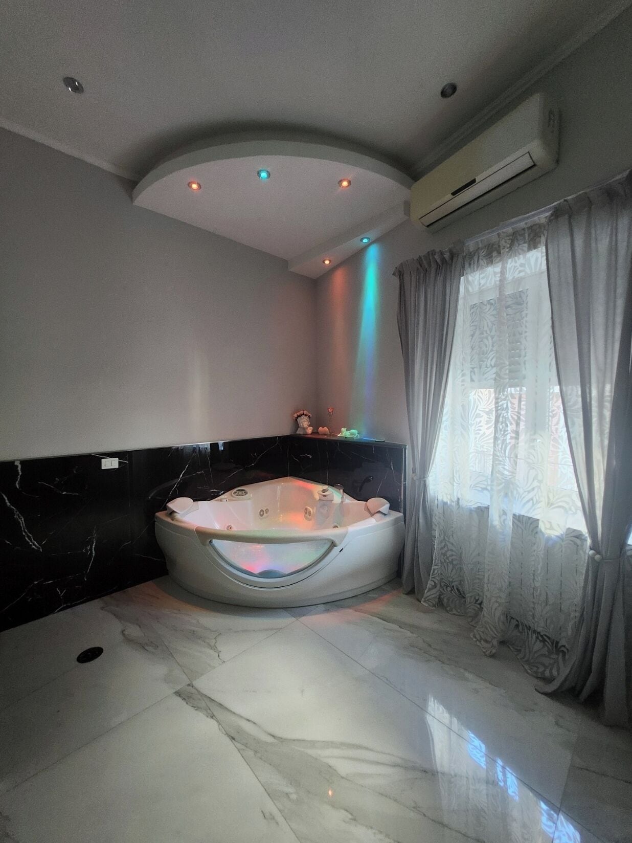 Ein modernes Badezimmer mit einer freistehenden Badewanne, Marmorboden und einem großen Fenster mit Vorhängen.