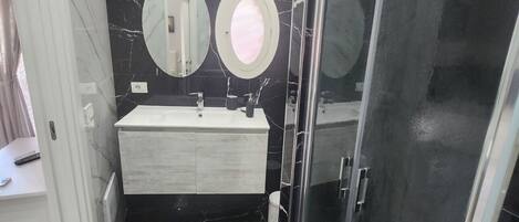 A modern bathroom with a black marble floor, a white vanity, two round mirrors, and a glass-enclosed shower area.