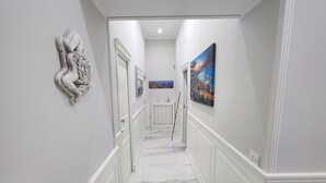 A hallway with marble flooring, white walls, and a red fire extinguisher.