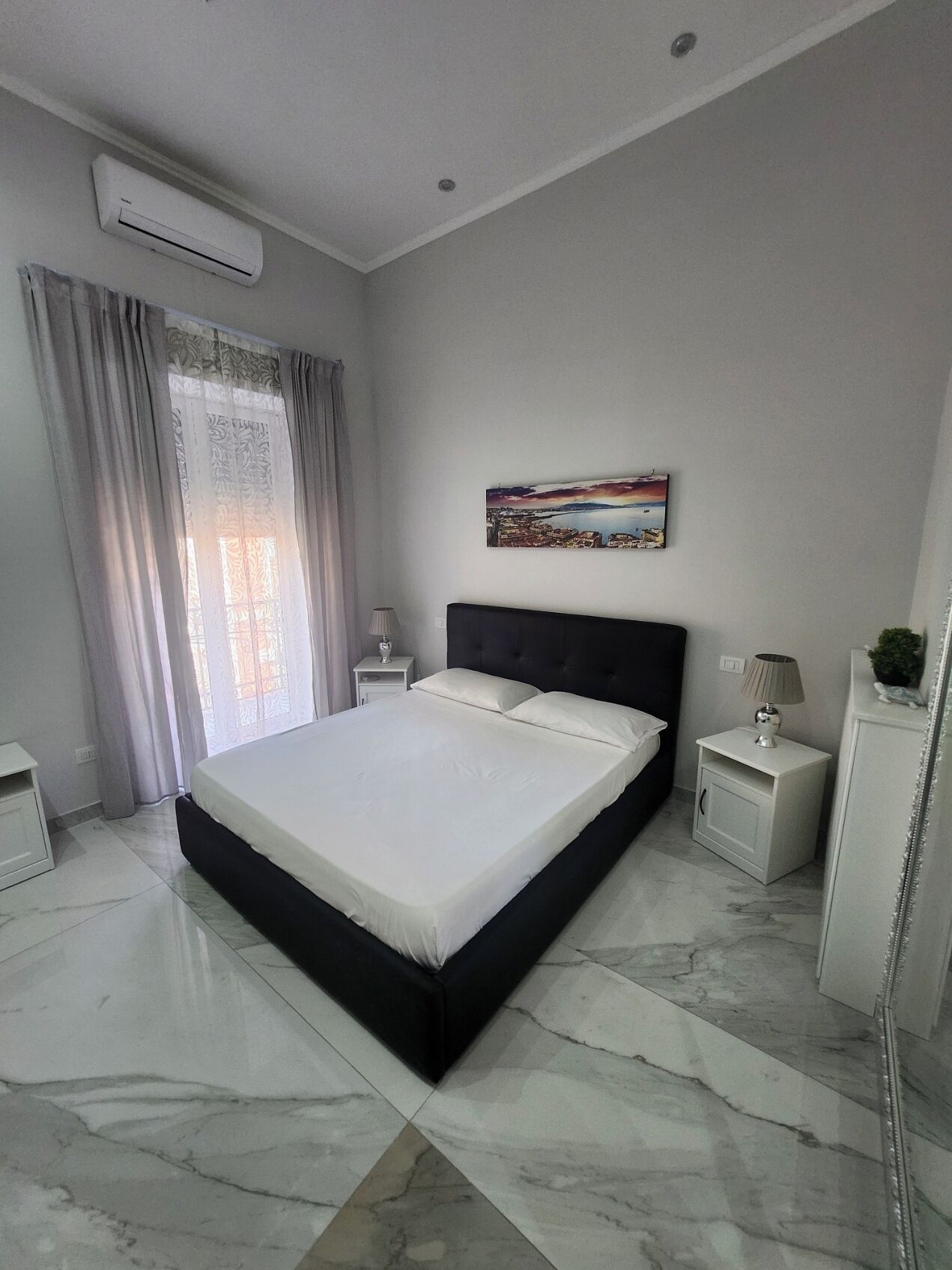 A modern bedroom with a large bed, a nightstand, a lamp, and a painting on the wall.