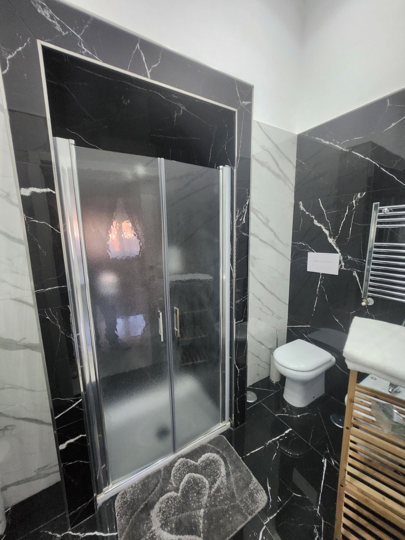 A modern bathroom with a glass-enclosed shower, a white toilet, and a marble-tiled floor.