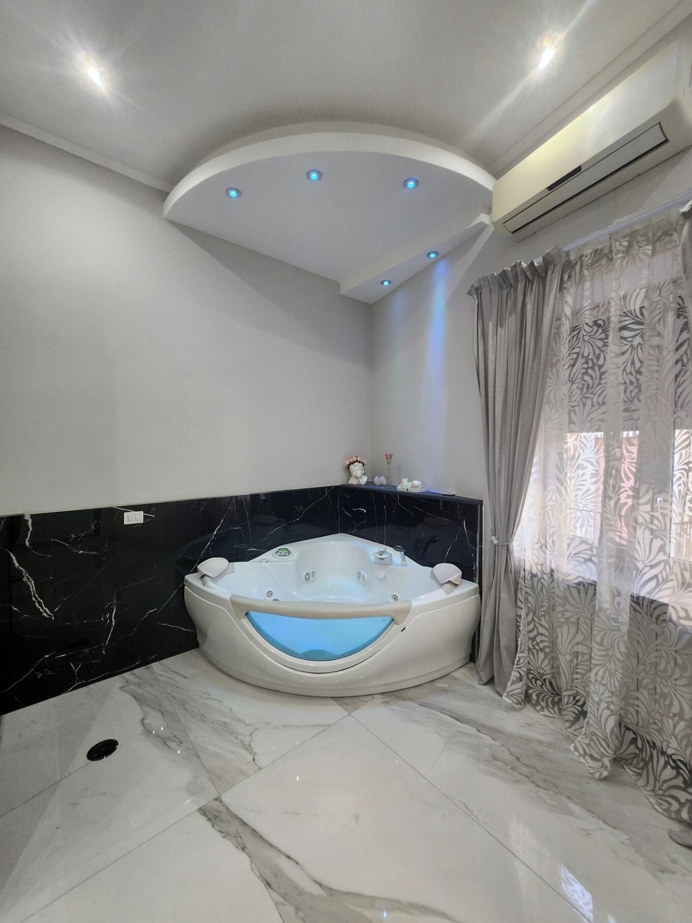 Een moderne badkamer met een vrijstaand bad, marmeren vloeren en een plafond met inbouwverlichting.