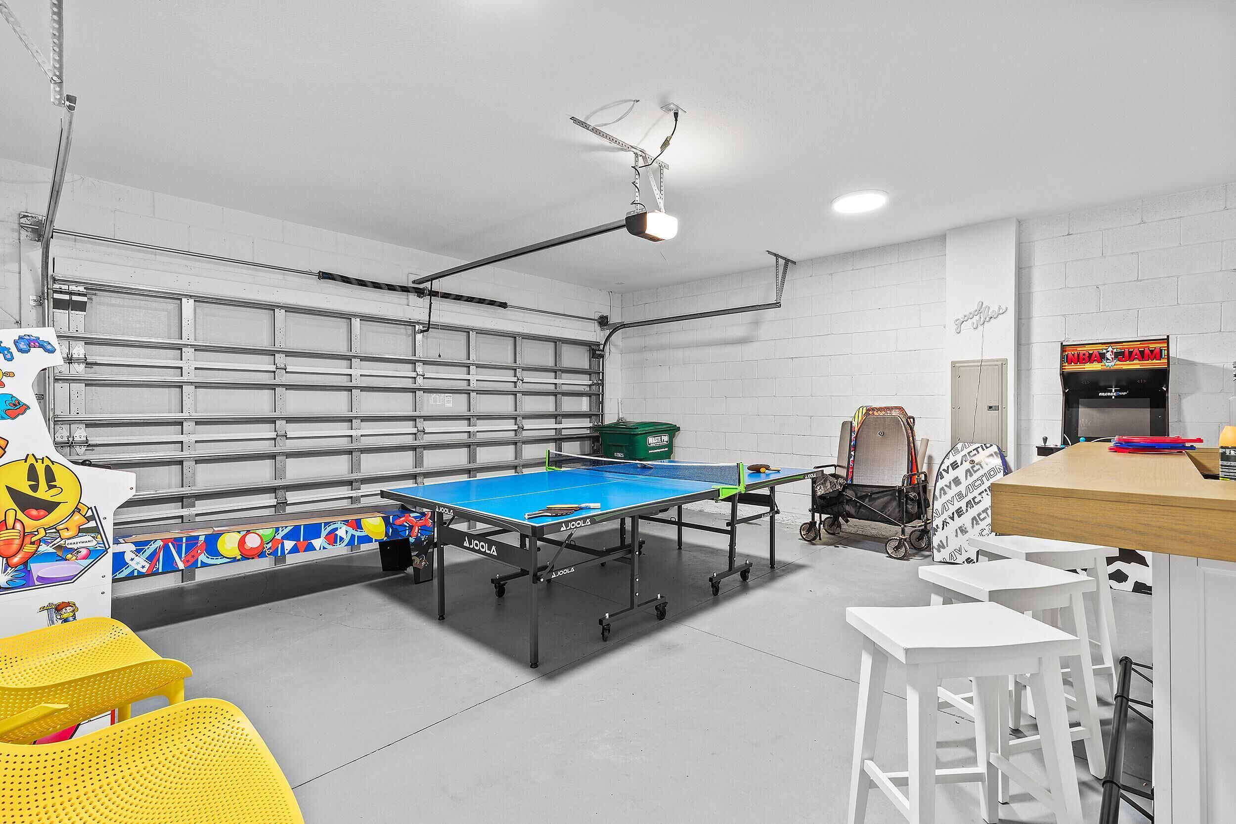 A ping pong table in a room with white walls, a ceiling light, and a small table with chairs.