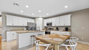A modern kitchen with white cabinets, a wooden island, and a dining table with four chairs. - Oceans 25- Lazy Beach Days (Daytona Beach)