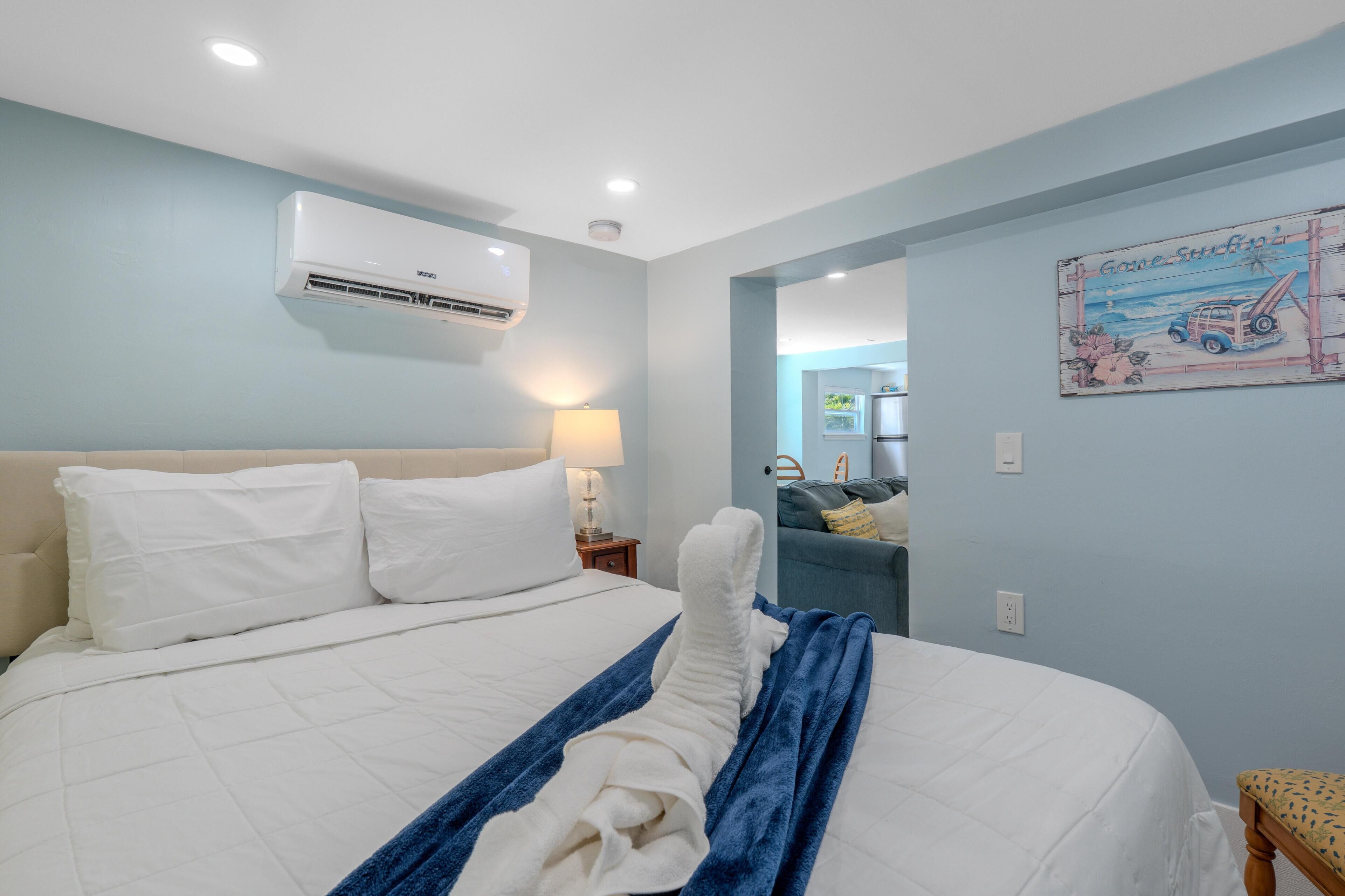 A hotel room with a bed, a wall-mounted air conditioner, a lamp, and a beach-themed wall decoration.