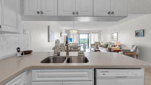 A modern kitchen with white cabinetry, a double sink, and a built-in dishwasher. - Sea Club #402 - Isle Be Back (Indian Shores)
