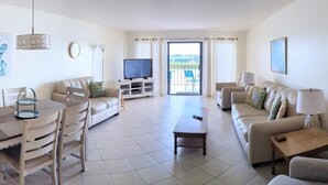 A spacious living room with a sofa, a coffee table, a TV, and a balcony with a view. - Sea Club #402 - Isle Be Back (Indian Shores)