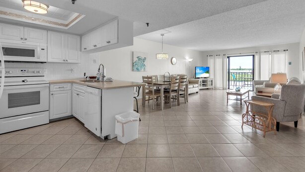 A modern kitchen with white cabinets, a built-in microwave, and a dining area with a wooden table and chairs. - Sea Club #402 - Isle Be Back (Indian Shores)