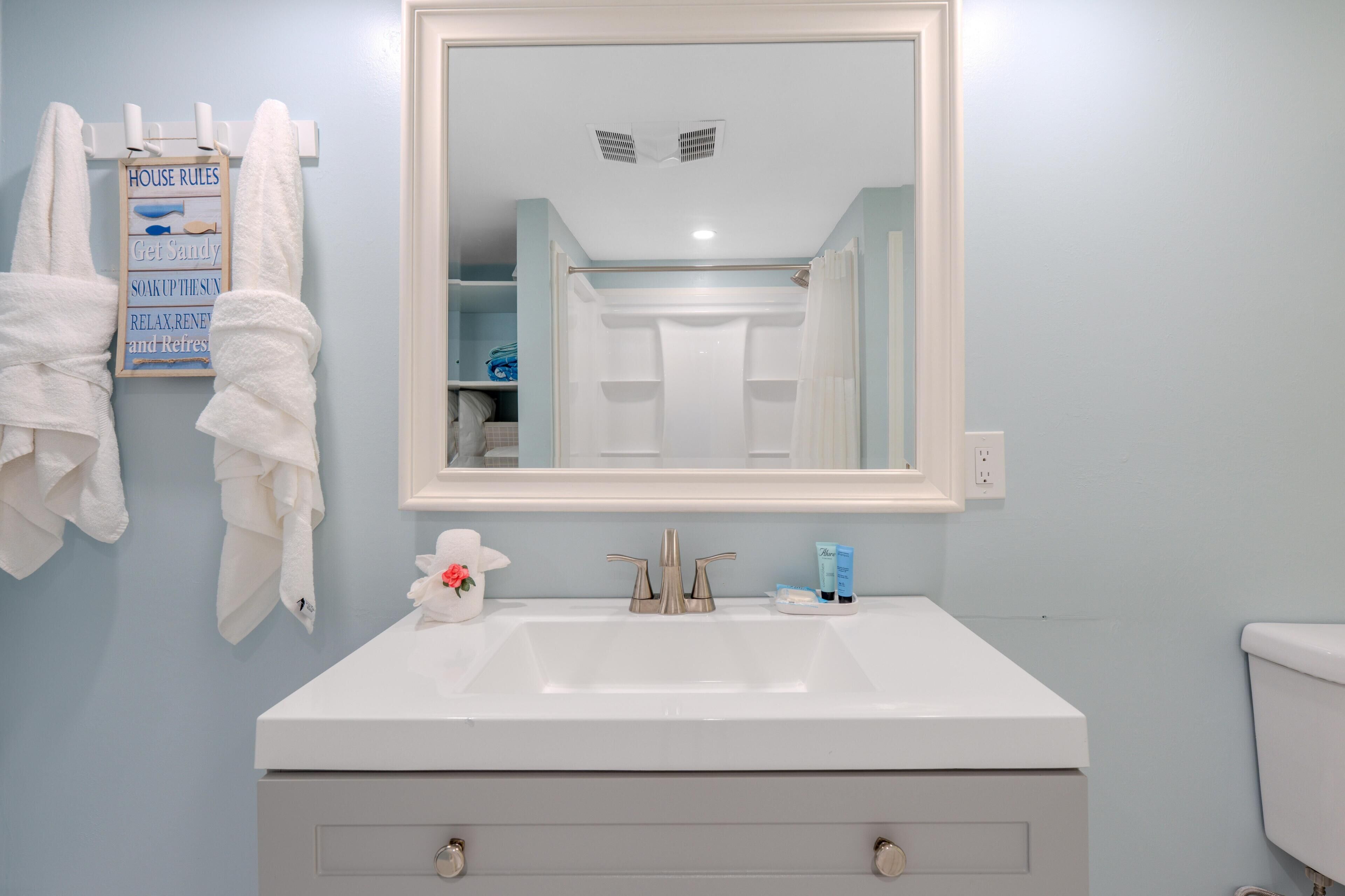 Un baño con lavamanos blanco, un espejo y toallas colgadas en un perchero.