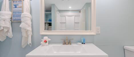 Un baño con lavamanos blanco, un espejo y toallas colgadas en un perchero.