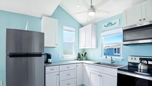 A kitchen with white cabinets, a stainless steel refrigerator, a black stove, and a window with a view of a house. - Island Paradise Estate (Fort Myers Beach)
