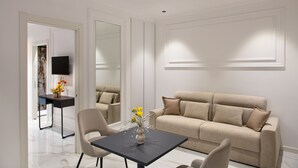 Una sala de estar moderna con un sofá color beige, una mesa de centro negra con un jarrón de flores, y un televisor de pantalla plana montado en la pared.