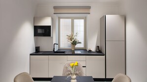 Una cocina moderna con encimera negra, armarios blancos, microondas integrado y refrigerador.