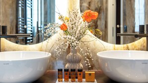 Un baño con dos lavamanos grandes blancos, un florero con flores y tres botellas de loción.
