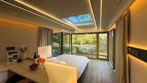 A modern hotel room with a large bed, a desk with a vase of flowers, and a view of the outdoors. - Space Camp (Interlachen)