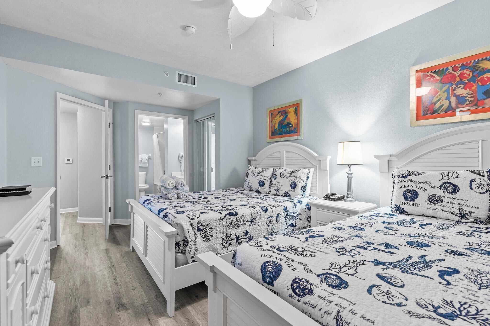 A bedroom with two beds, a nightstand, a dresser, and a door leading to another room.