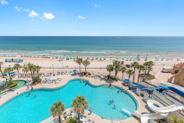 A resort with a large swimming pool, a beach area, and a water slide.