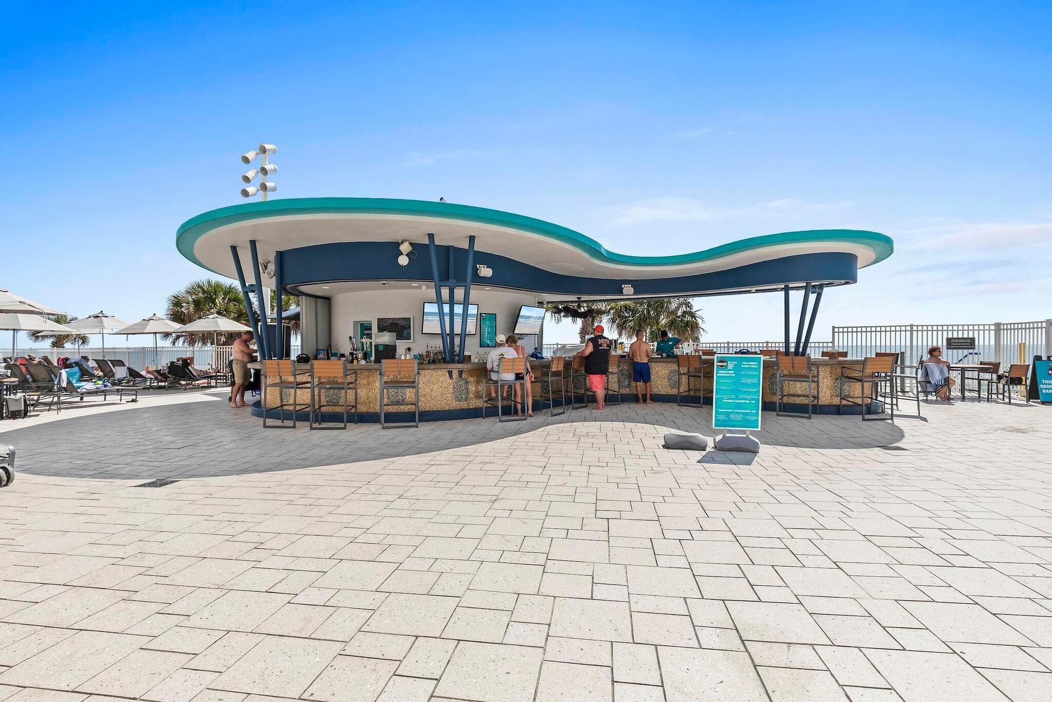 Ett kafé vid stranden med uteservering och en böjd takkonstruktion.