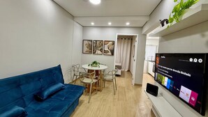 Un salon moderne avec un canapé bleu, un coin repas doté d’une table ronde et un téléviseur affichant l’interface de Netflix.