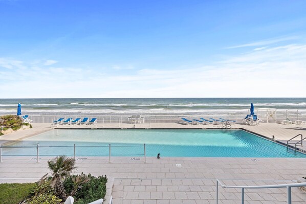 Relax by the serene pool surrounded by lounge chairs and umbrellas, with access to the beach.