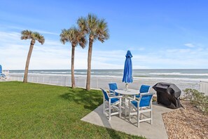 An outdoor patio with a table and chairs, a grill, and a view of the ocean. - Surfside Club 503 (Daytona Beach Shores)