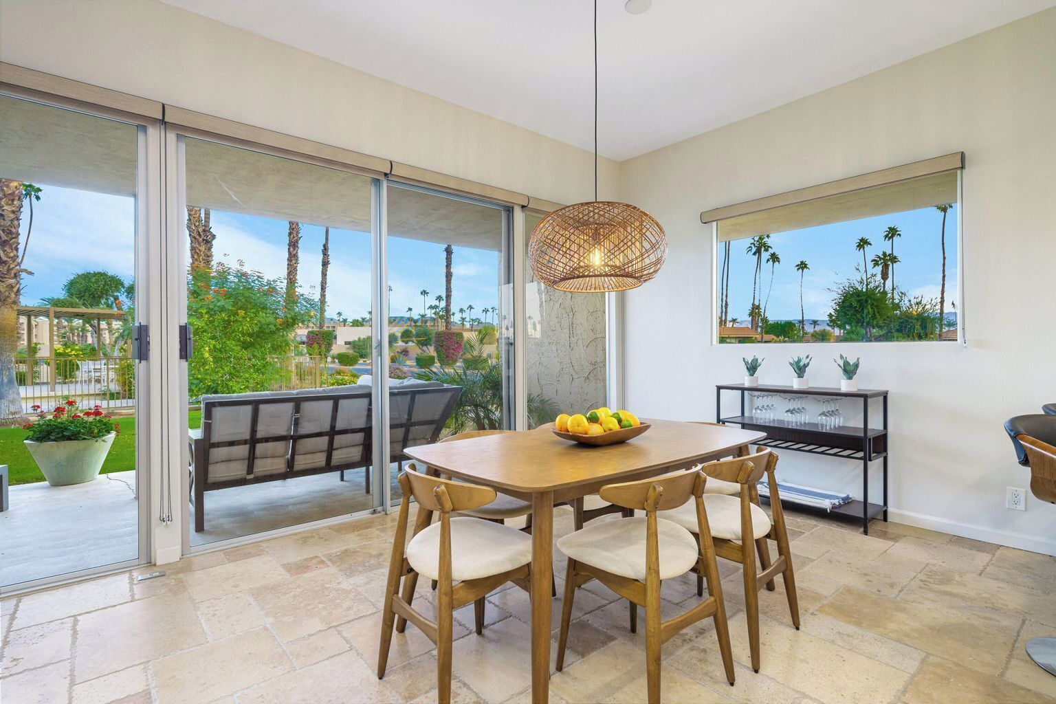 A modern dining area with a wooden table and chairs, a hanging light fixture, and a view of a garden through glass doors.