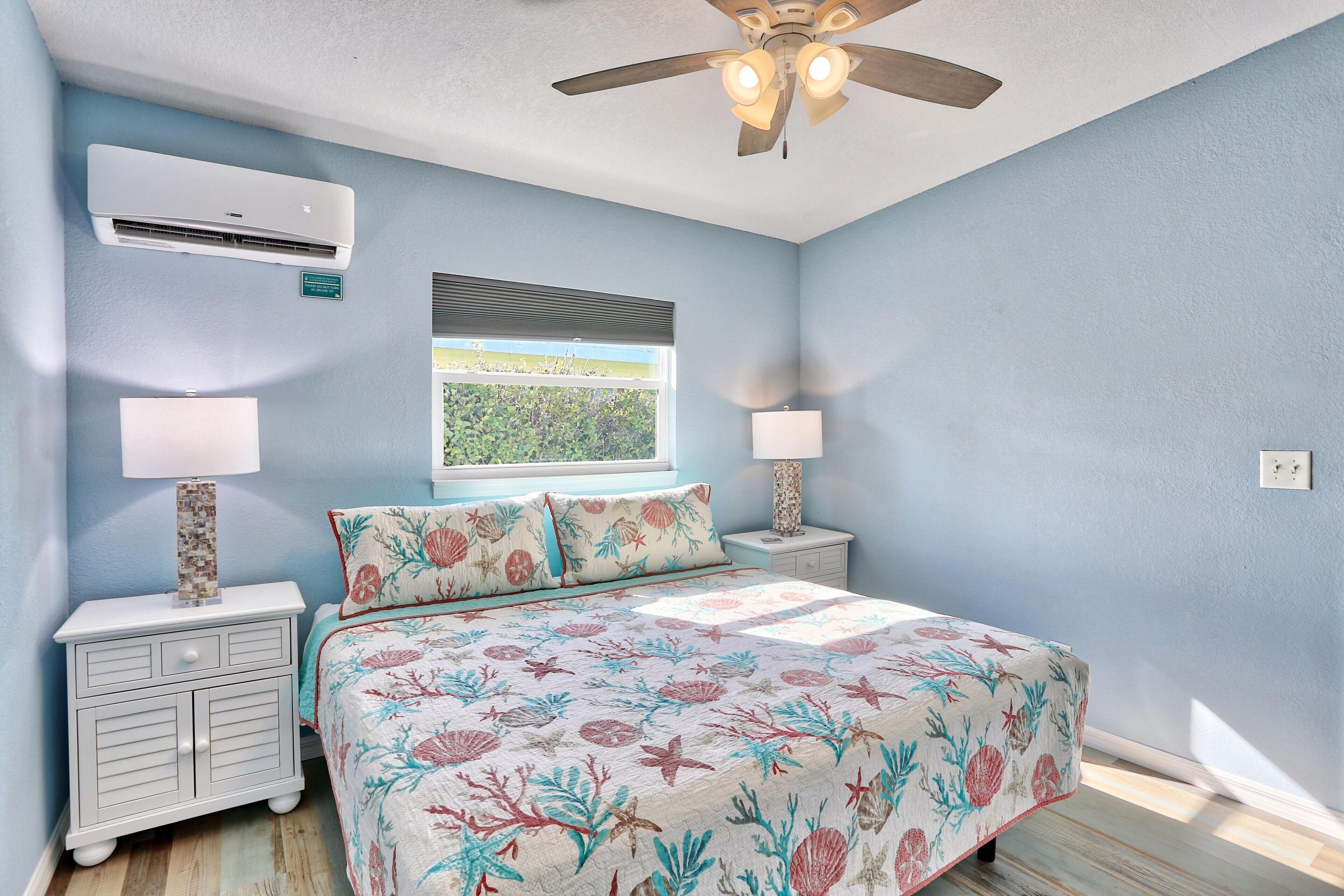 A bedroom with a bed, nightstands, a ceiling fan, an air conditioner, and a window with blinds.