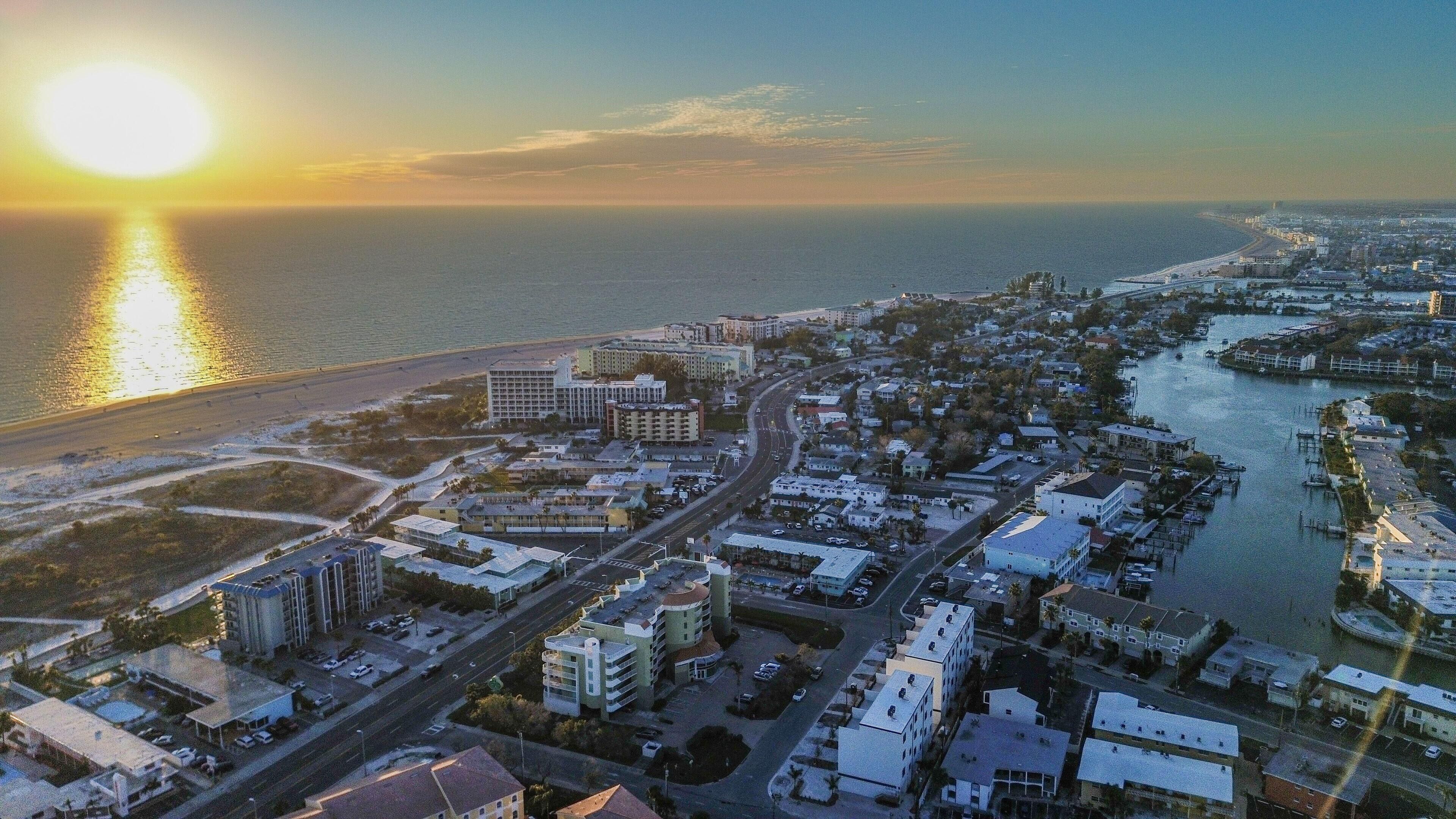 An aerial view of a coastal city with a beach, marina, and dense urban area.