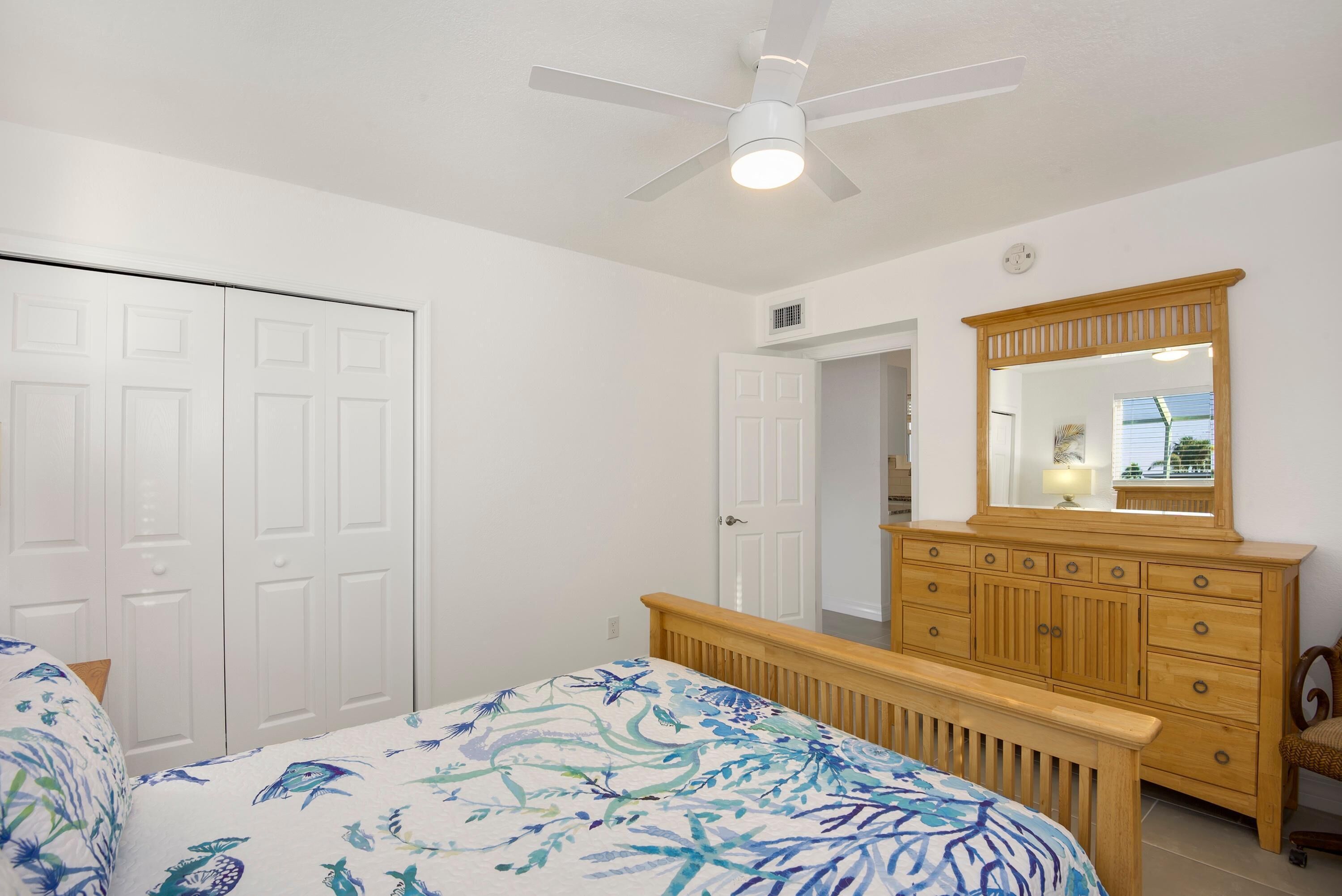 A bedroom with a bed, a wooden dresser, a ceiling fan, and a white door.