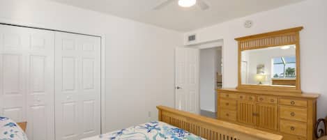 A bedroom with a bed, a wooden dresser, a ceiling fan, and a white door.
